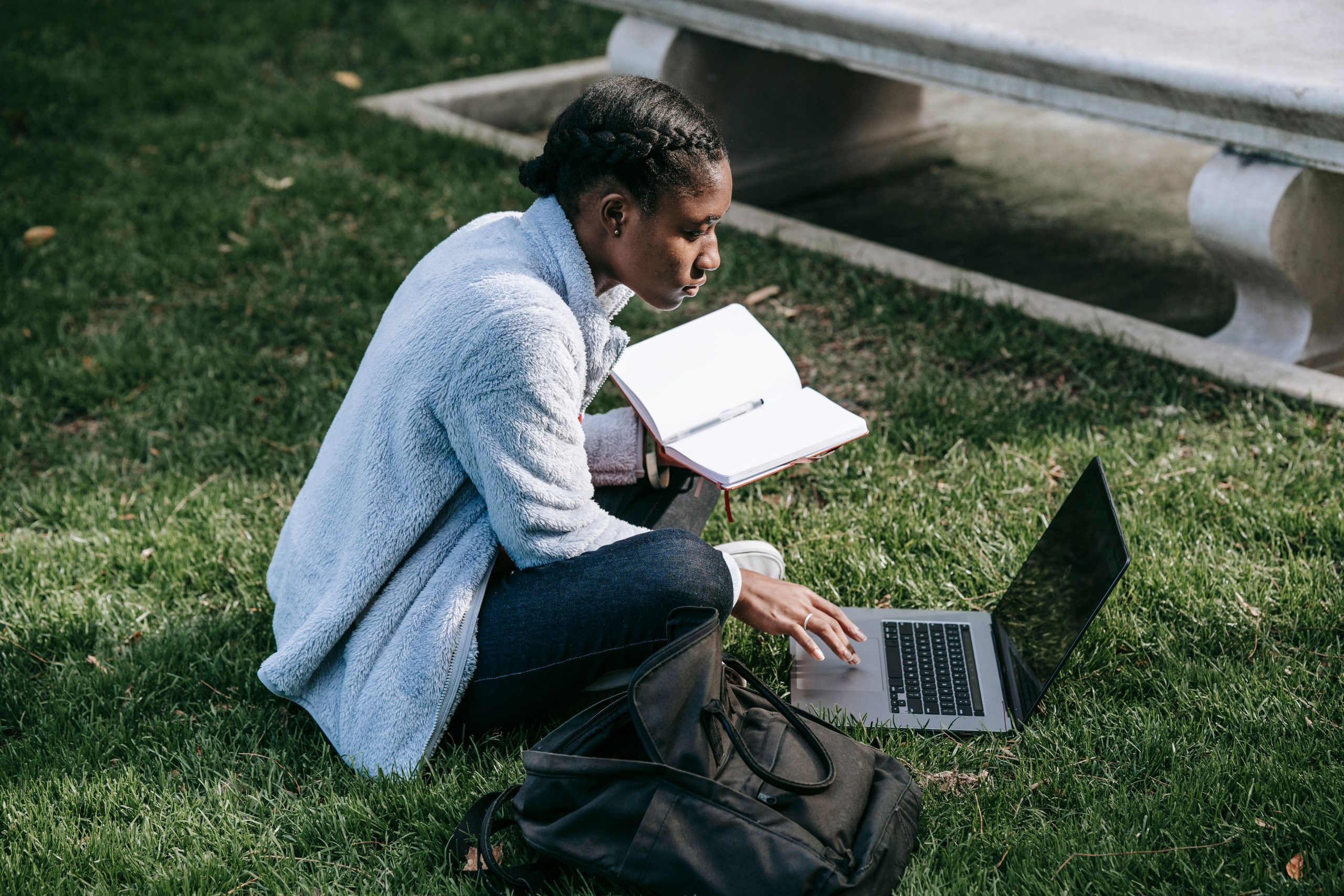 College student taking notes and working on a laptop outdoors on campus