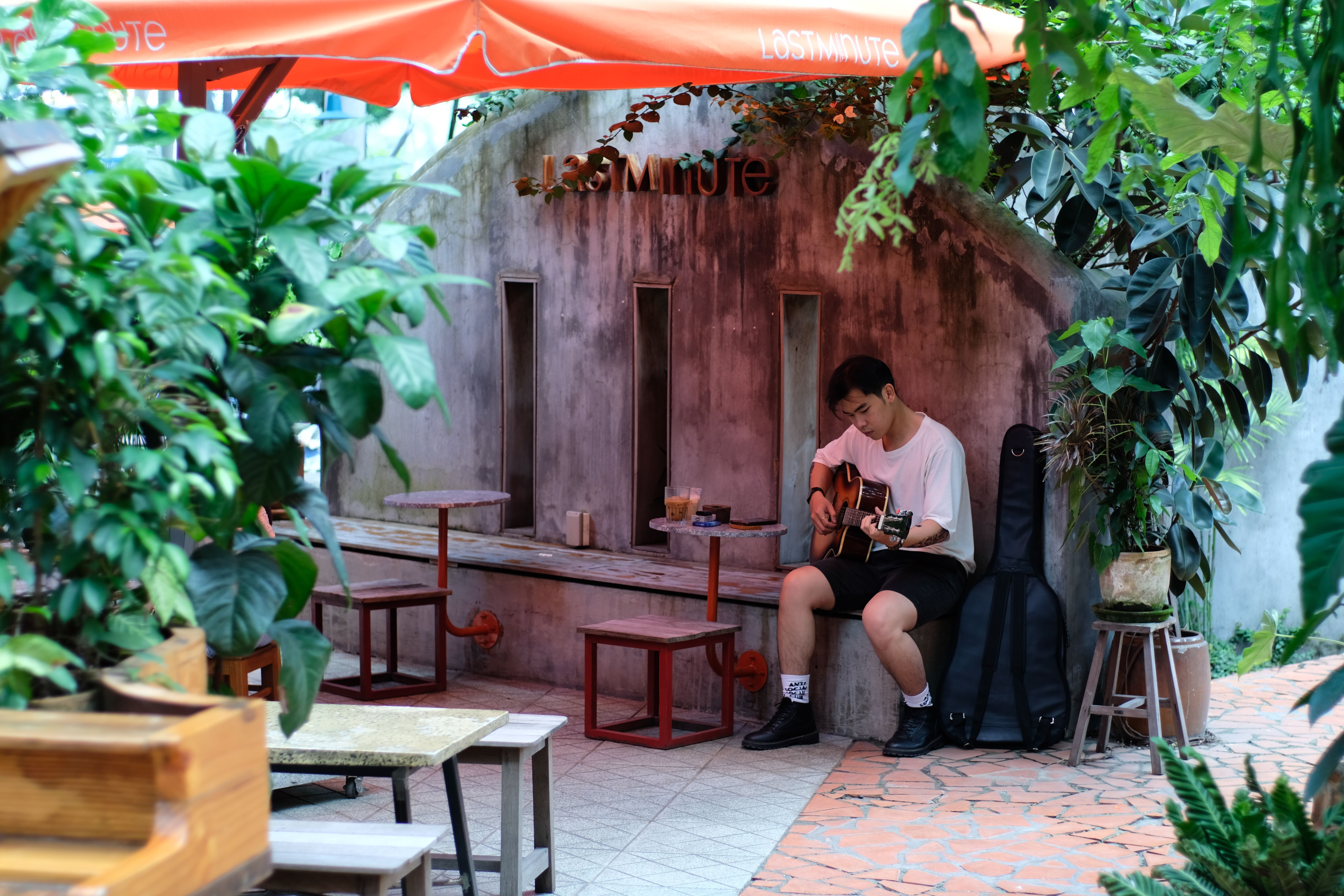 Musician playing acoustic guitar at a leafy outdoor cafe