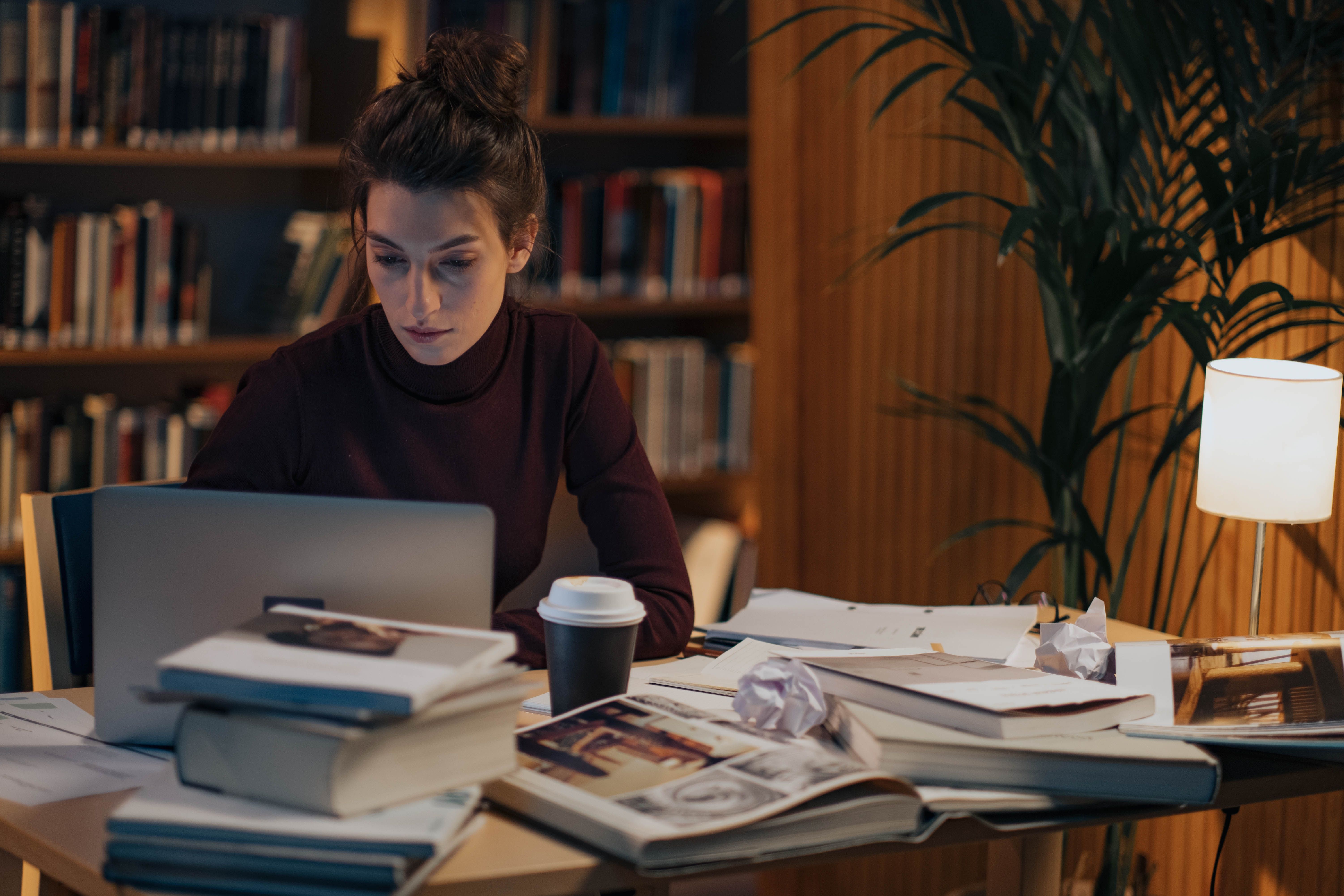 Woman working late on a laptop surrounded by books and coffee